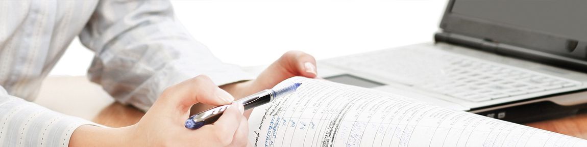 Une personne écrit sur un morceau de papier devant un ordinateur portable.