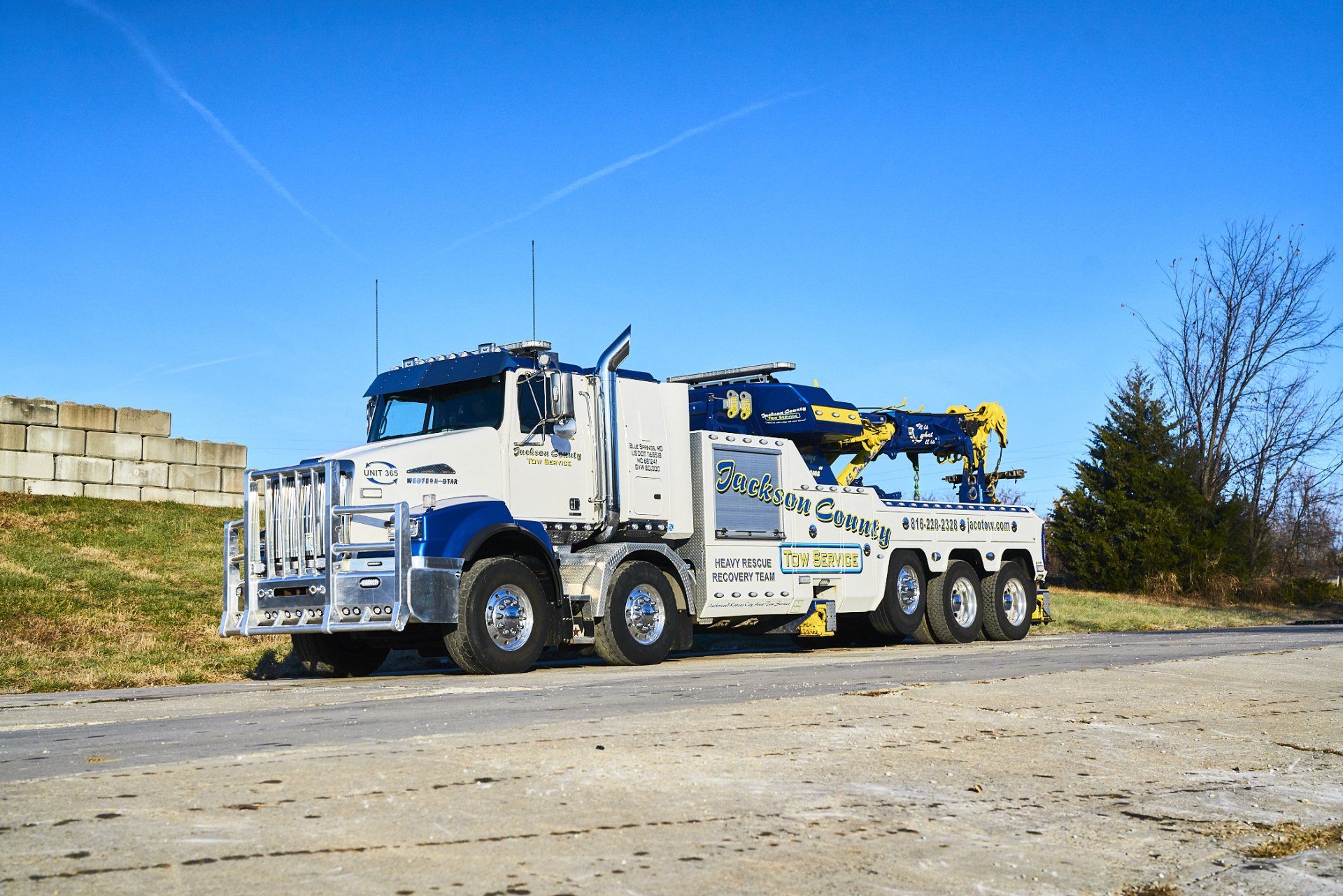 White tow truck with blue crane parked on a gravel road under a clear blue sky