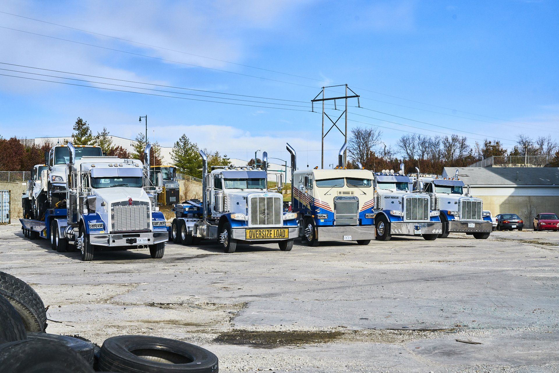 Row of white tow trucks parked in a lot under a blue sky with power lines overhead