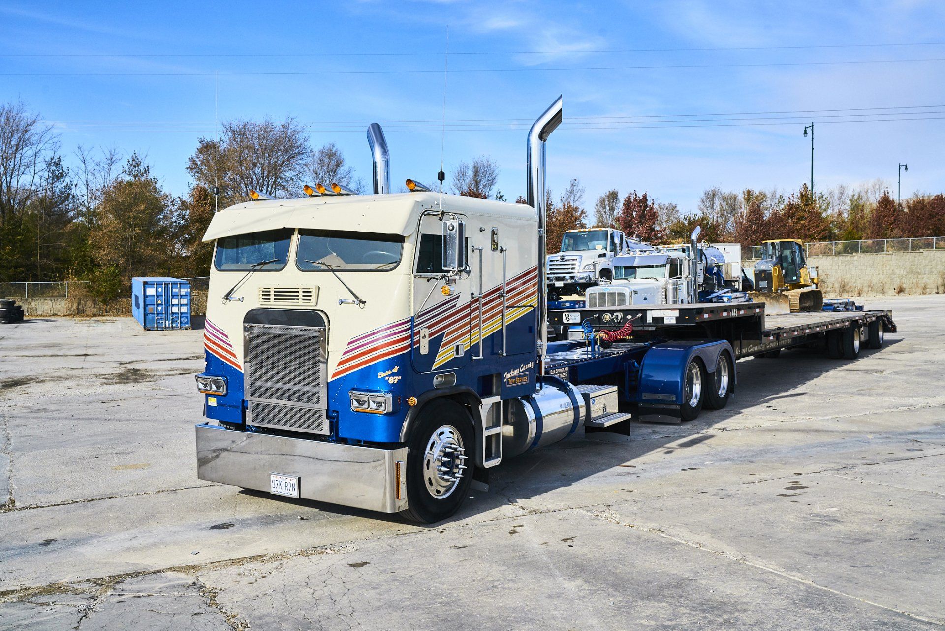 Blue and white semi truck hauling a flatbed trailer in a parking lot