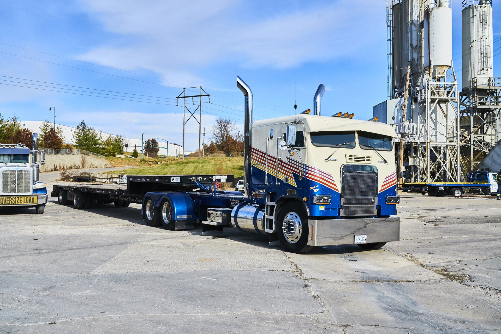 Flatbed truck with blue cab parked in an industrial yard under a clear sky