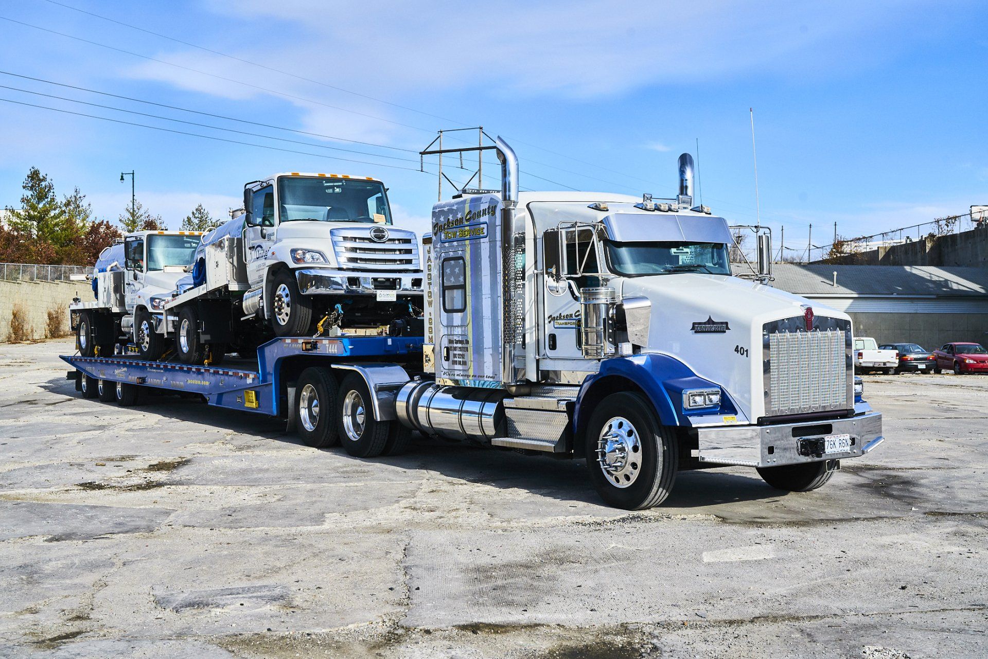 White semi-truck hauling a heavy-duty truck on a flatbed trailer in a lot