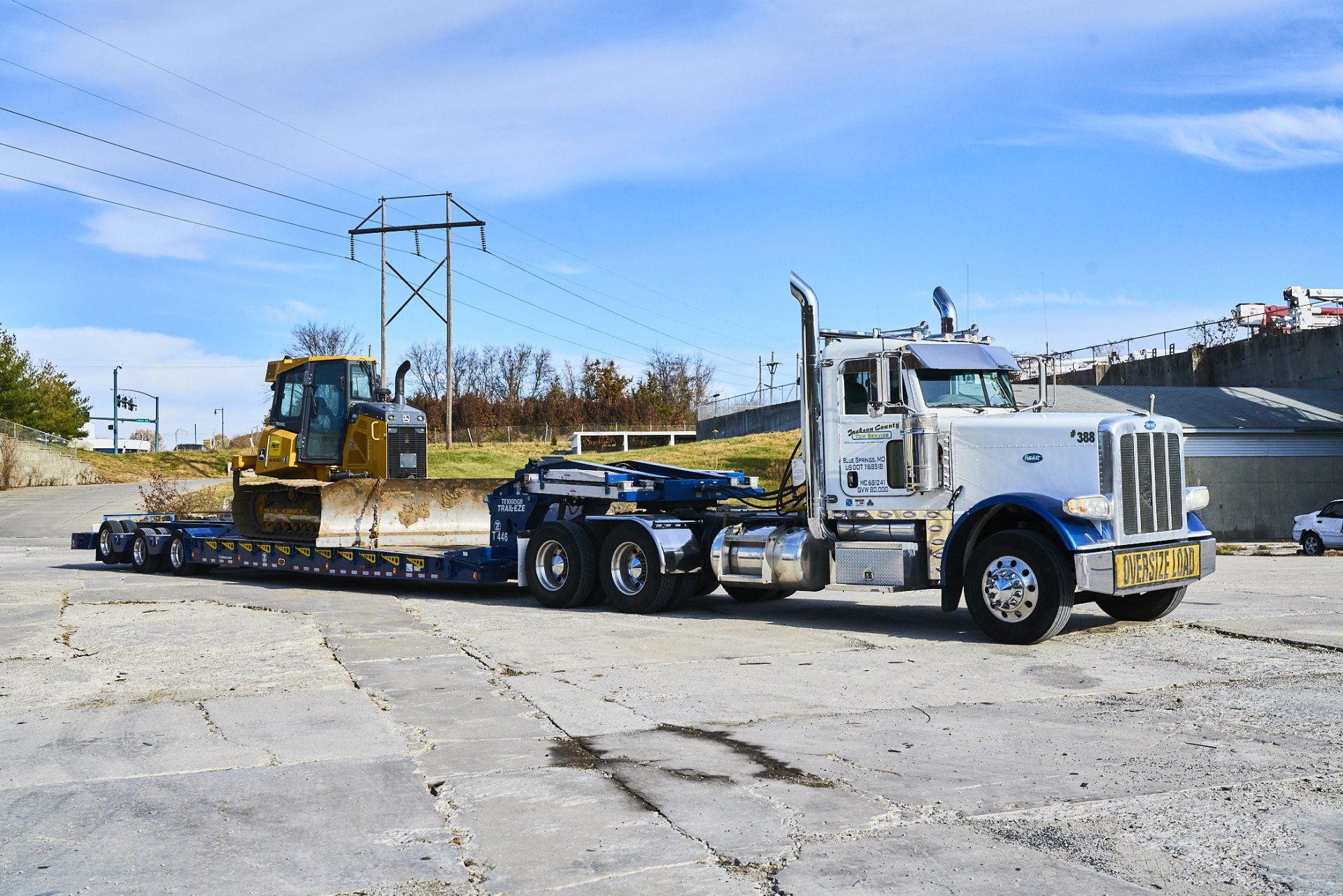 White tow truck hauling a yellow bulldozer on a flatbed trailer in an open lot