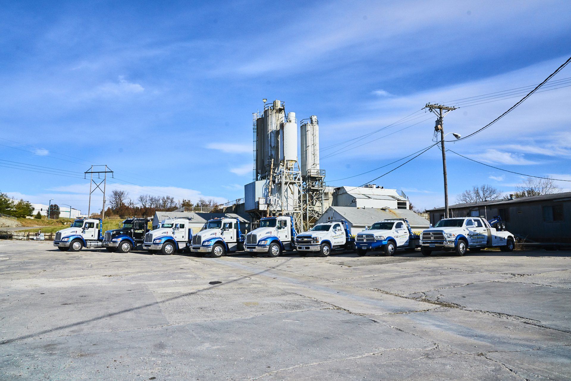 Fleet of blue-and-white utility trucks parked outside an industrial facility under a clear blue sky