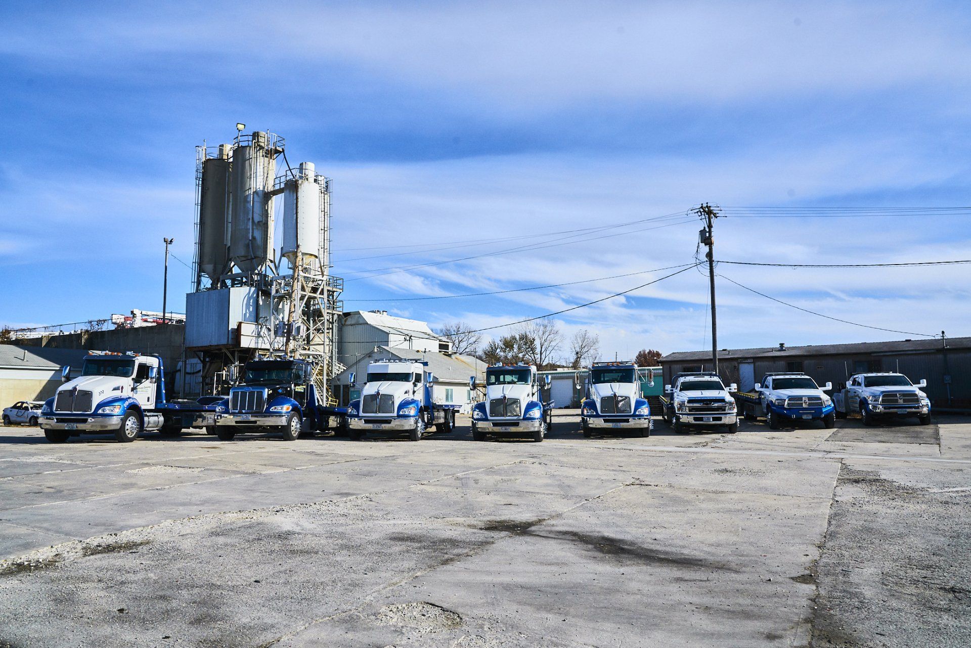 White trucks lined up outside an industrial plant under a blue sky.