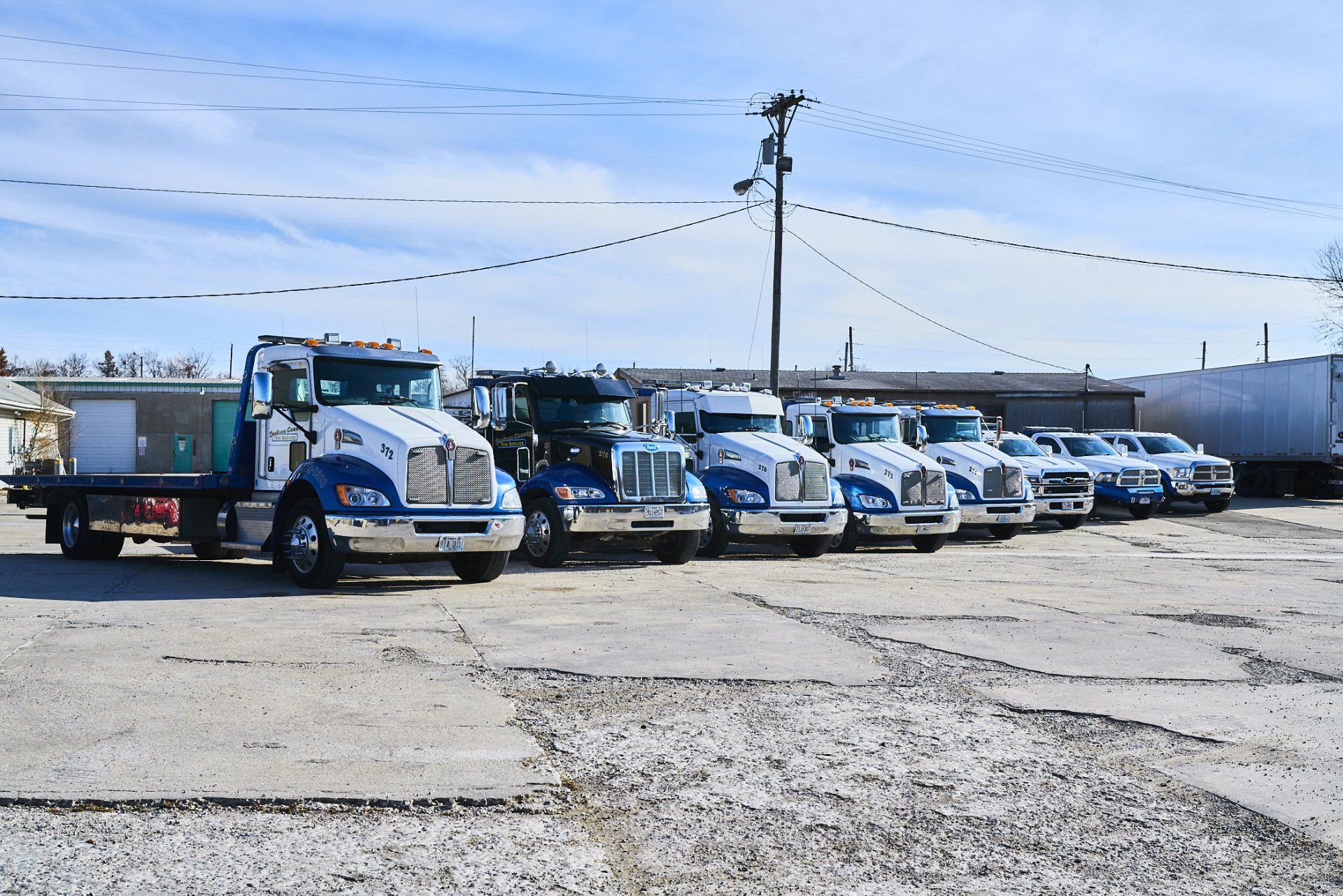 Row of white and blue work trucks parked in a gravel lot under a clear sky