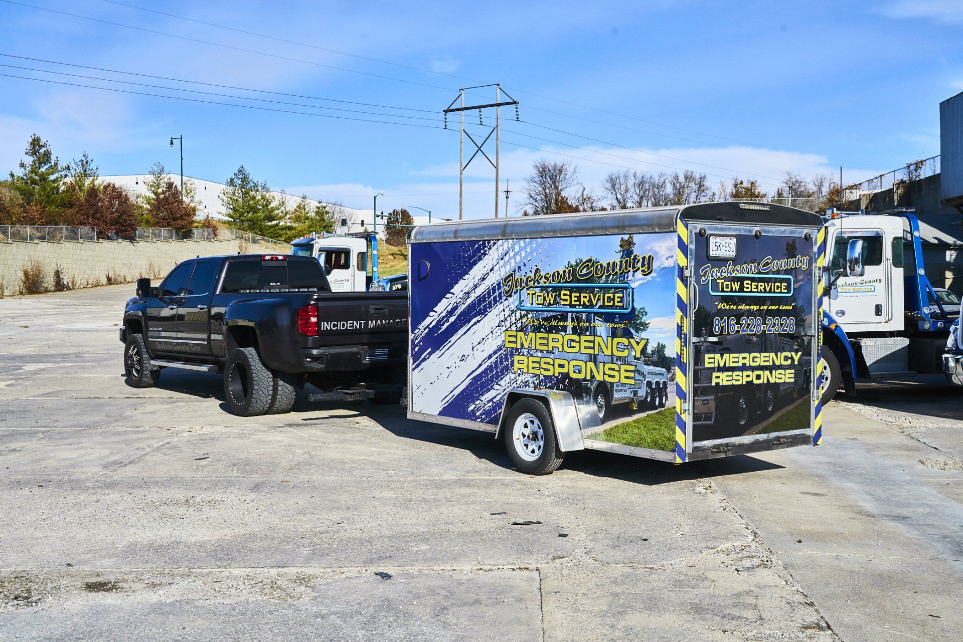 Black pickup towing a small advertising trailer in a parking lot under a clear blue sky
