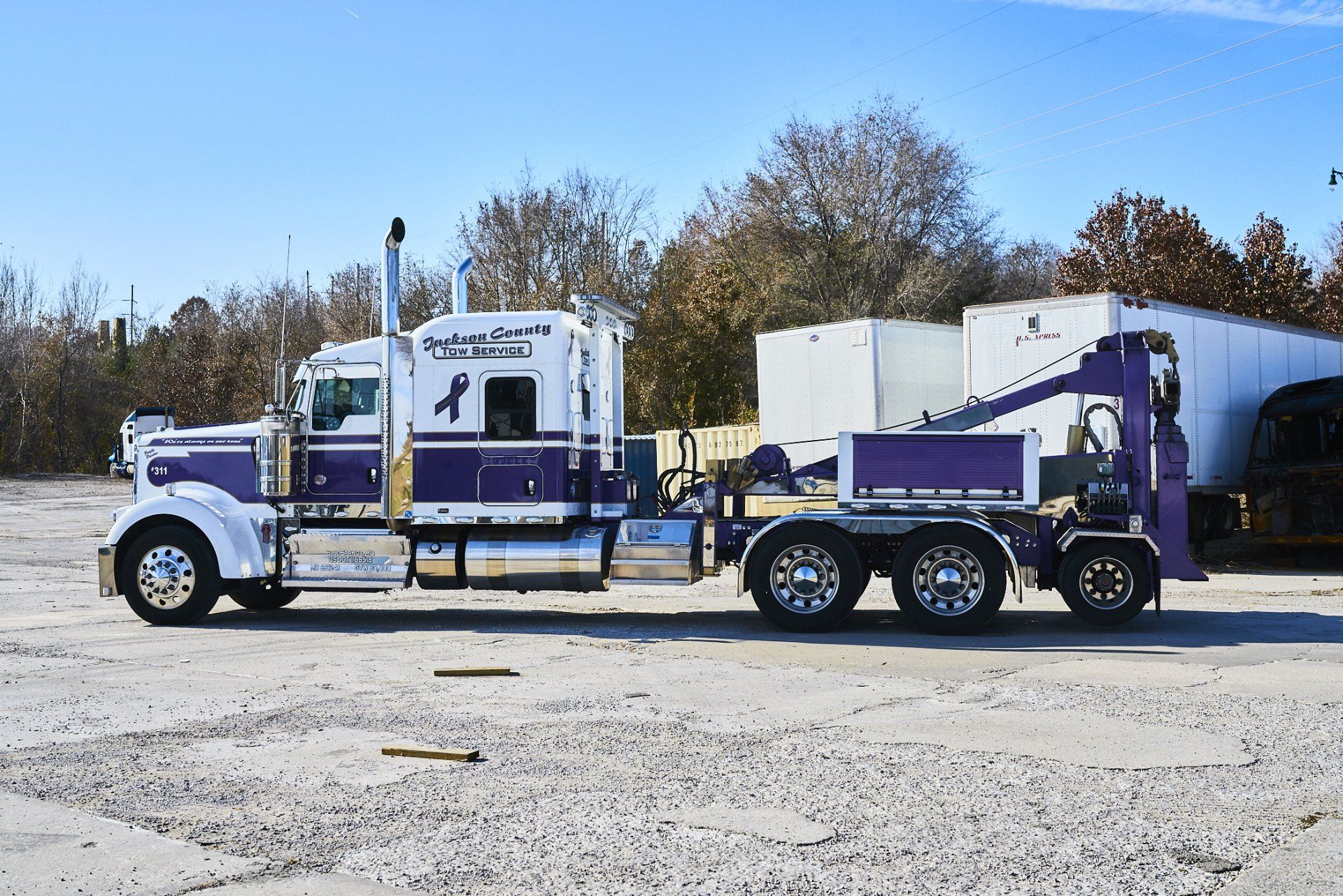 Two purple-and-white semi trucks parked side by side on a snowy lot under a clear sky