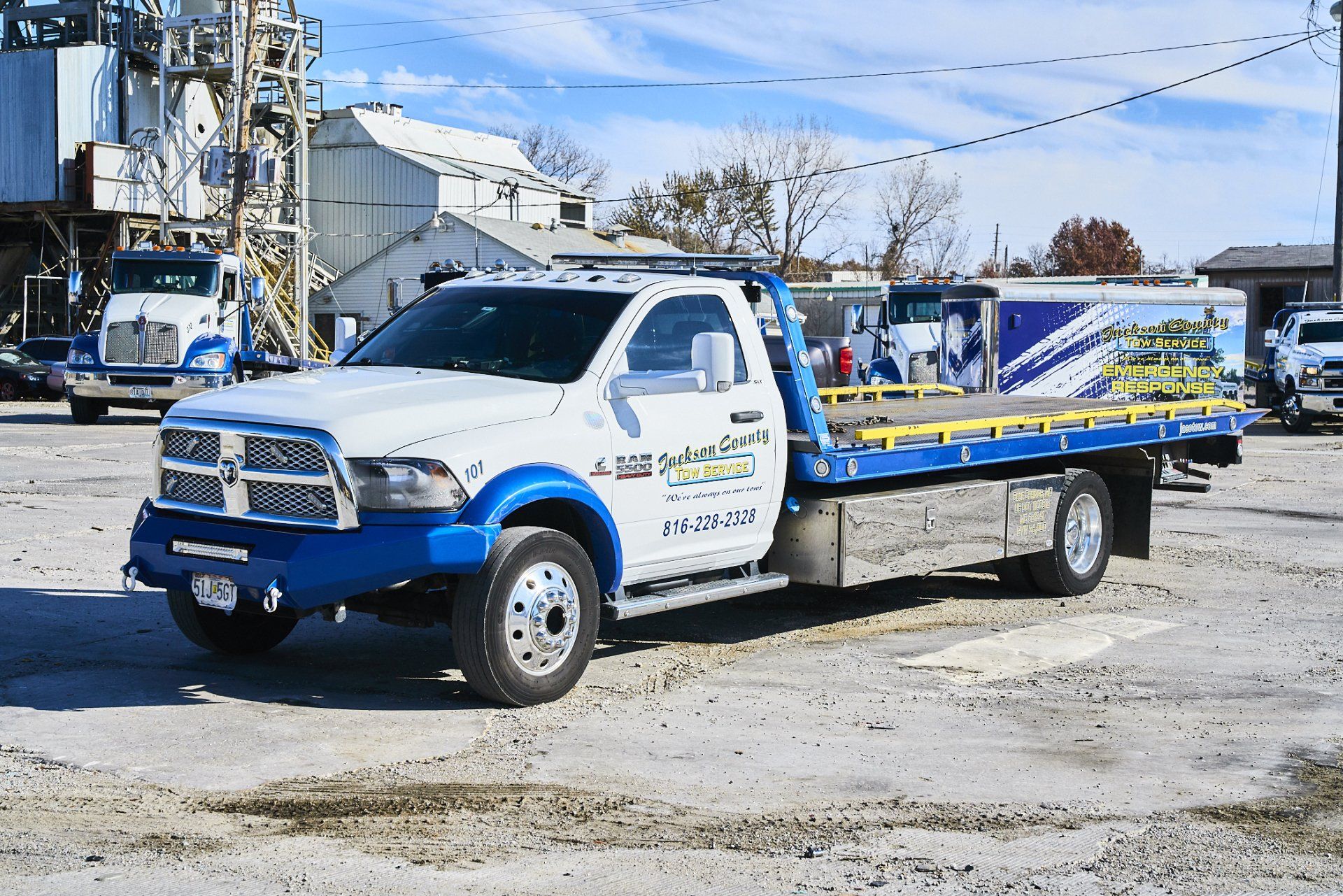 White and blue flatbed tow truck parked on a gravel lot under a clear sky