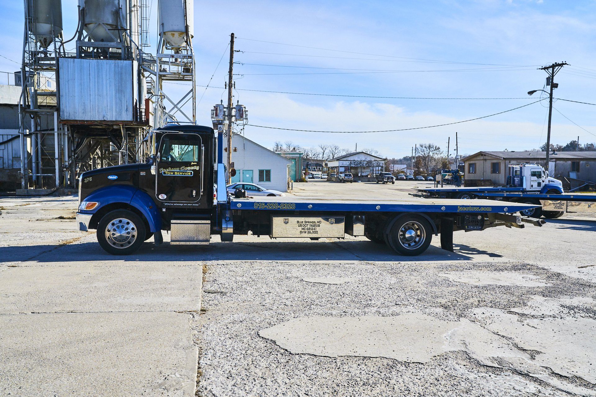 Blue flatbed tow truck parked in an industrial lot under a clear sky