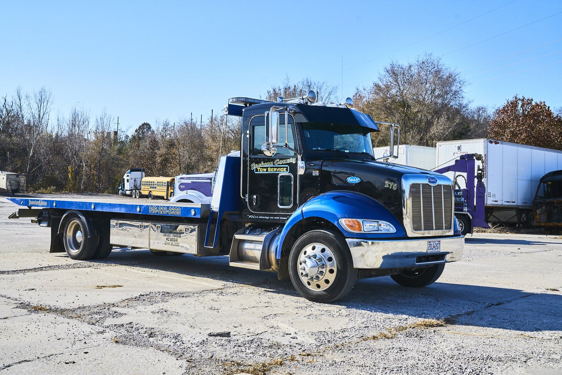 Blue tow truck parked on a gravel lot under a clear sky
