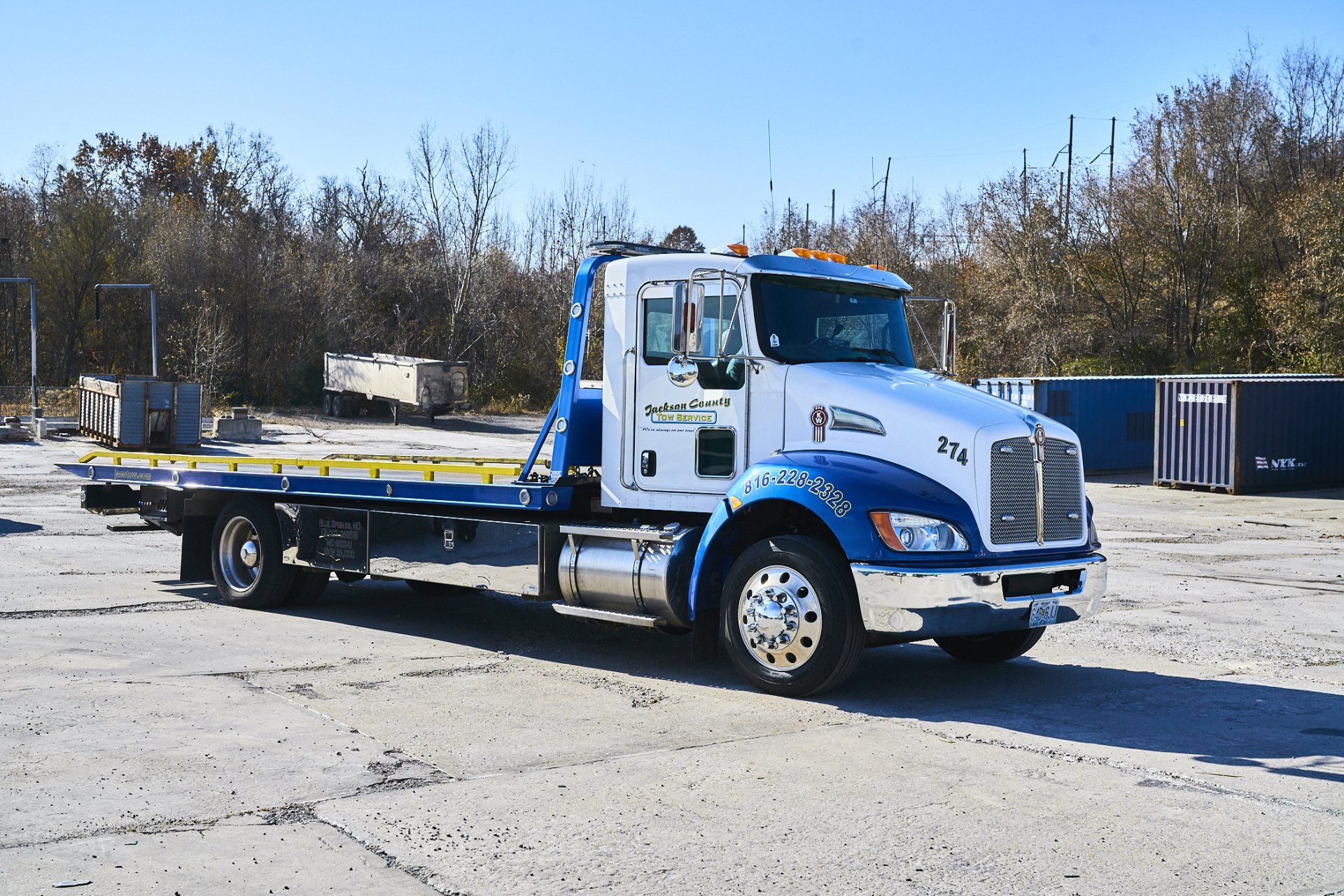 Blue and white flatbed tow truck parked in an open lot under a clear sky