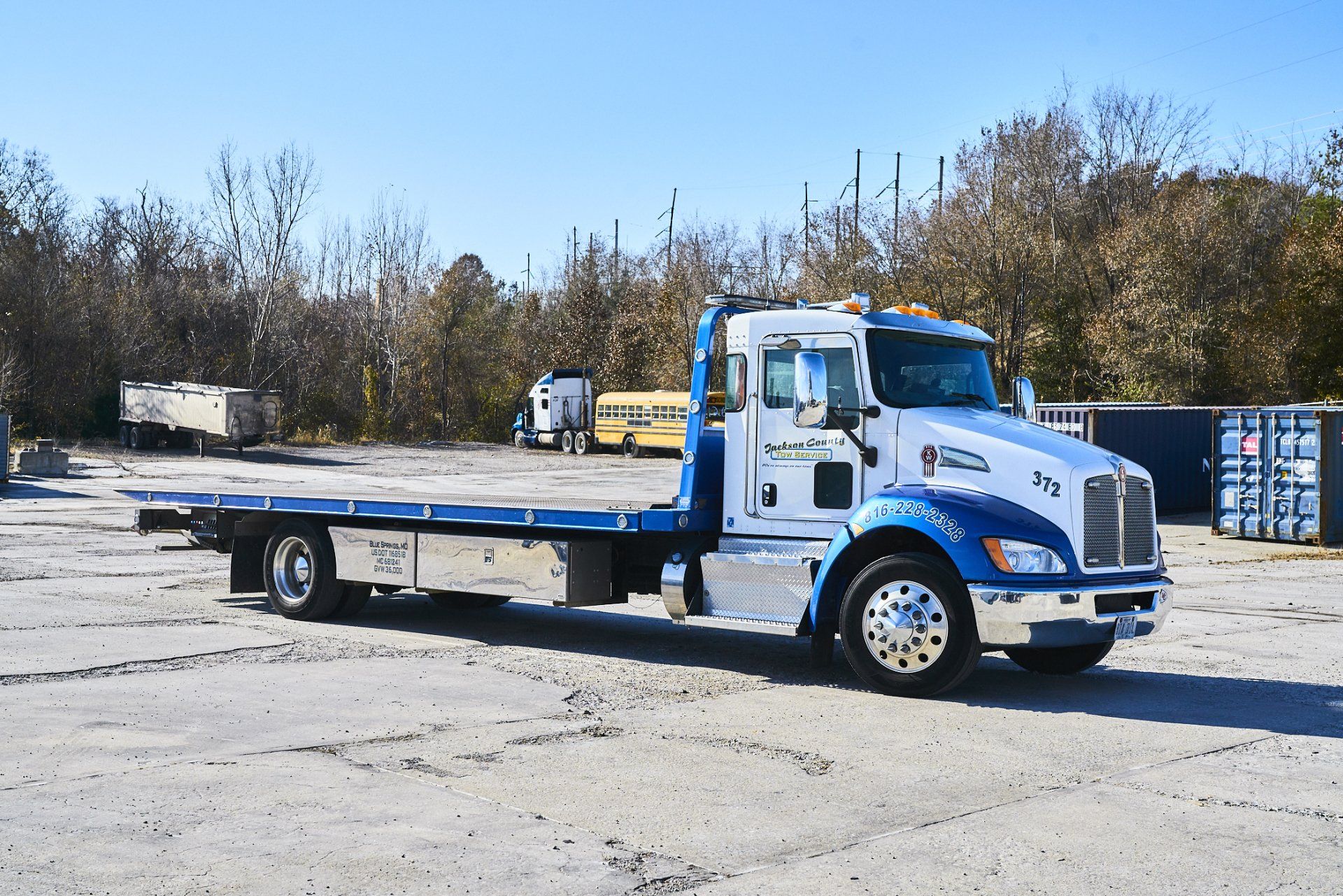 Blue flatbed tow truck parked on a gravel lot under a clear sky
