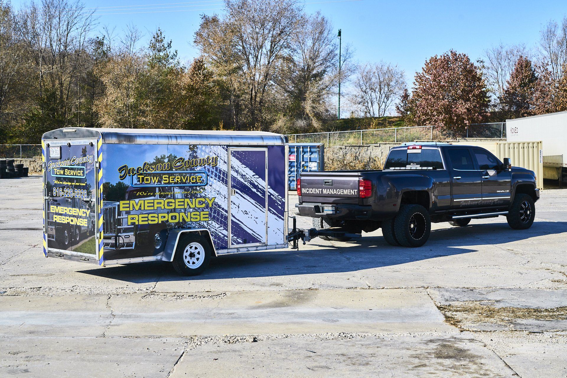 Black pickup towing a blue enclosed trailer in a parking lot on a sunny day