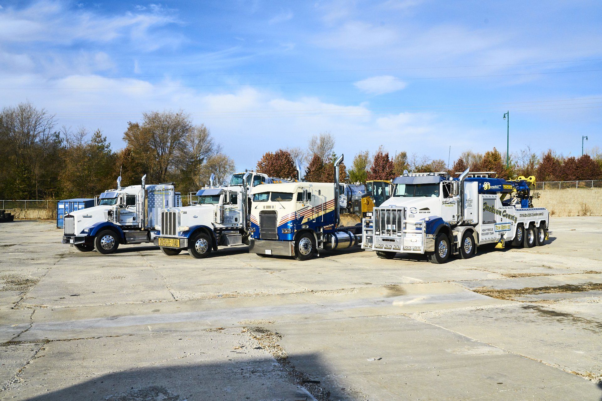 Three white tow trucks parked in a lot on a clear day