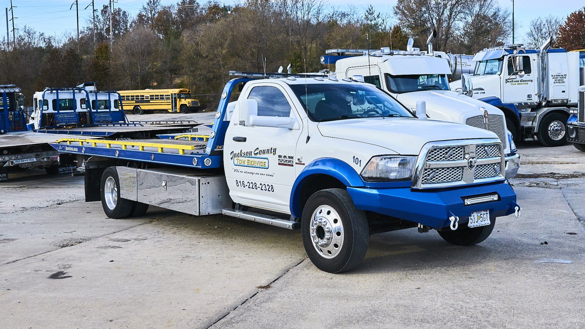 Blue-and-white tow truck parked in a lot with other trucks in the background