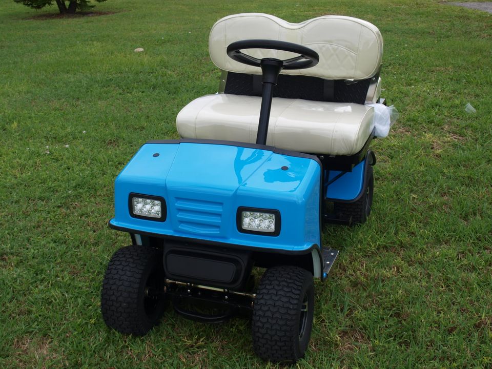 A blue and white golf cart is parked in the grass