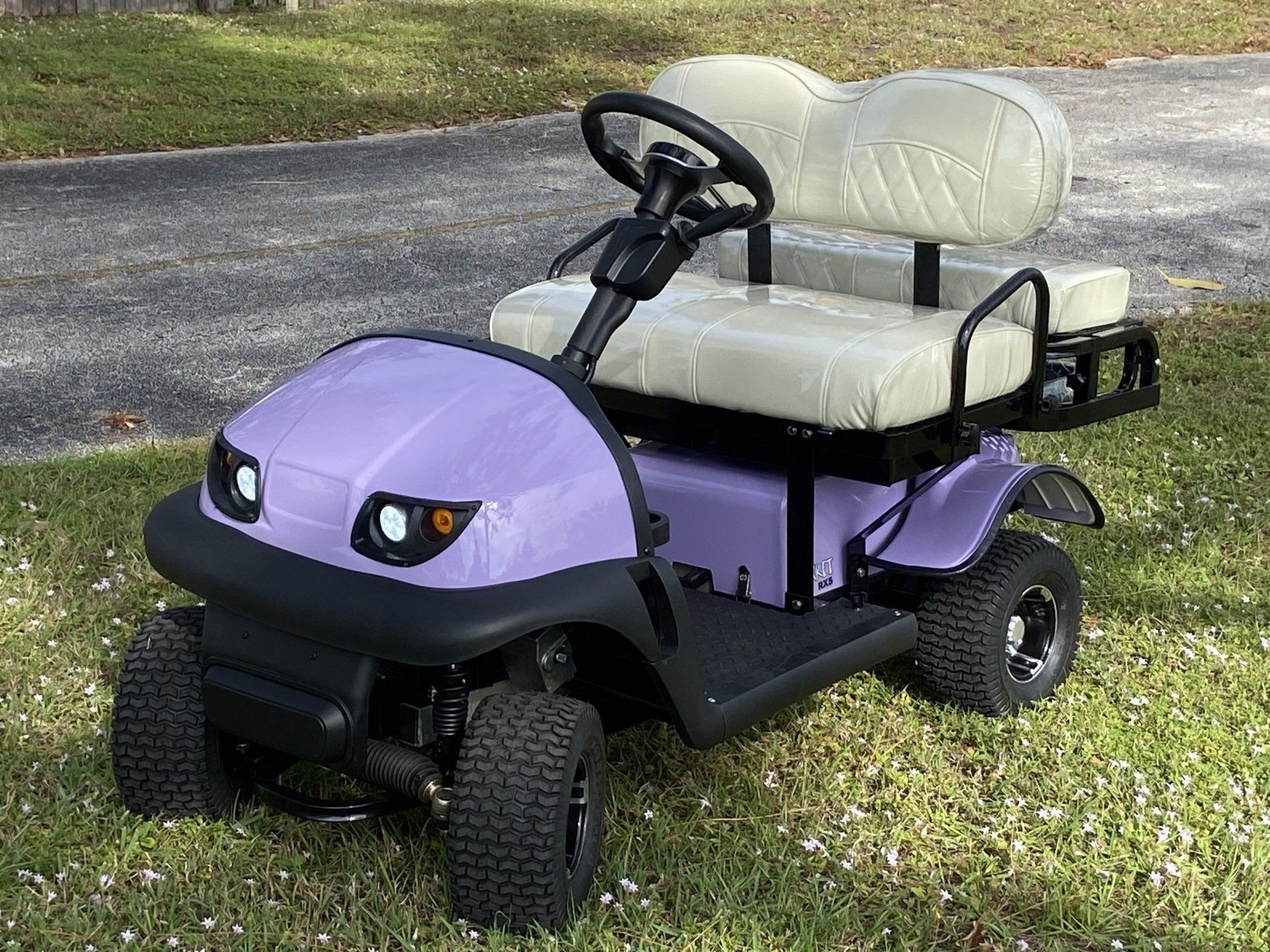 A purple golf cart is parked in the grass.