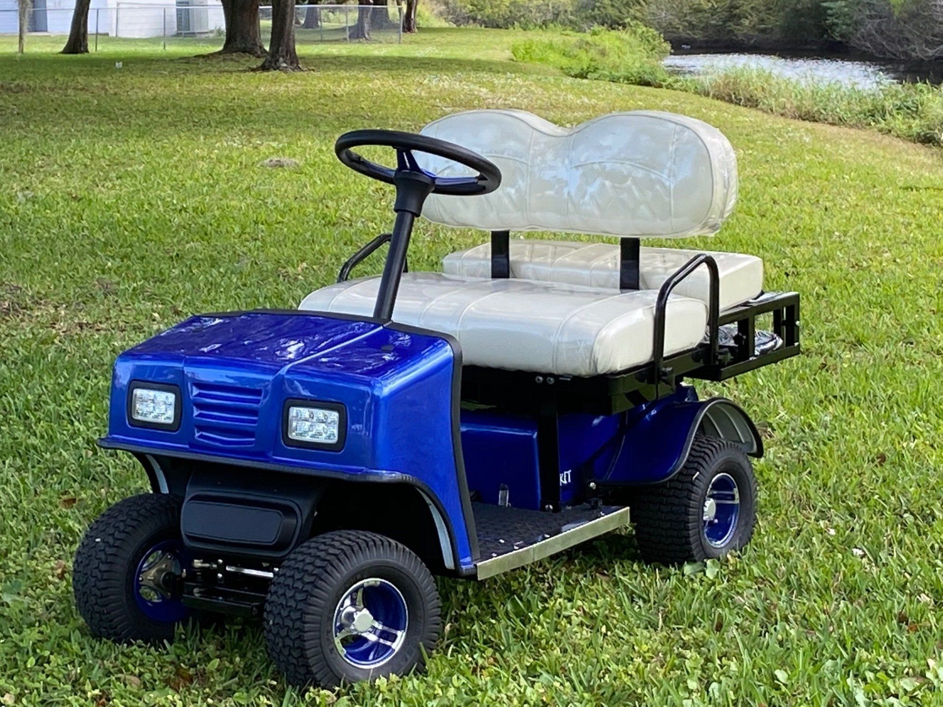 A blue golf cart with white seats is parked in the grass.