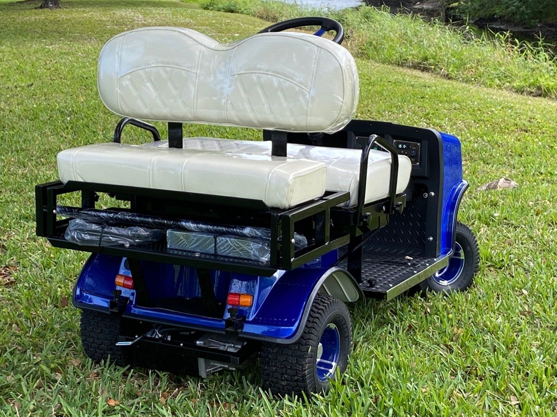 A blue golf cart with white seats is parked in the grass.
