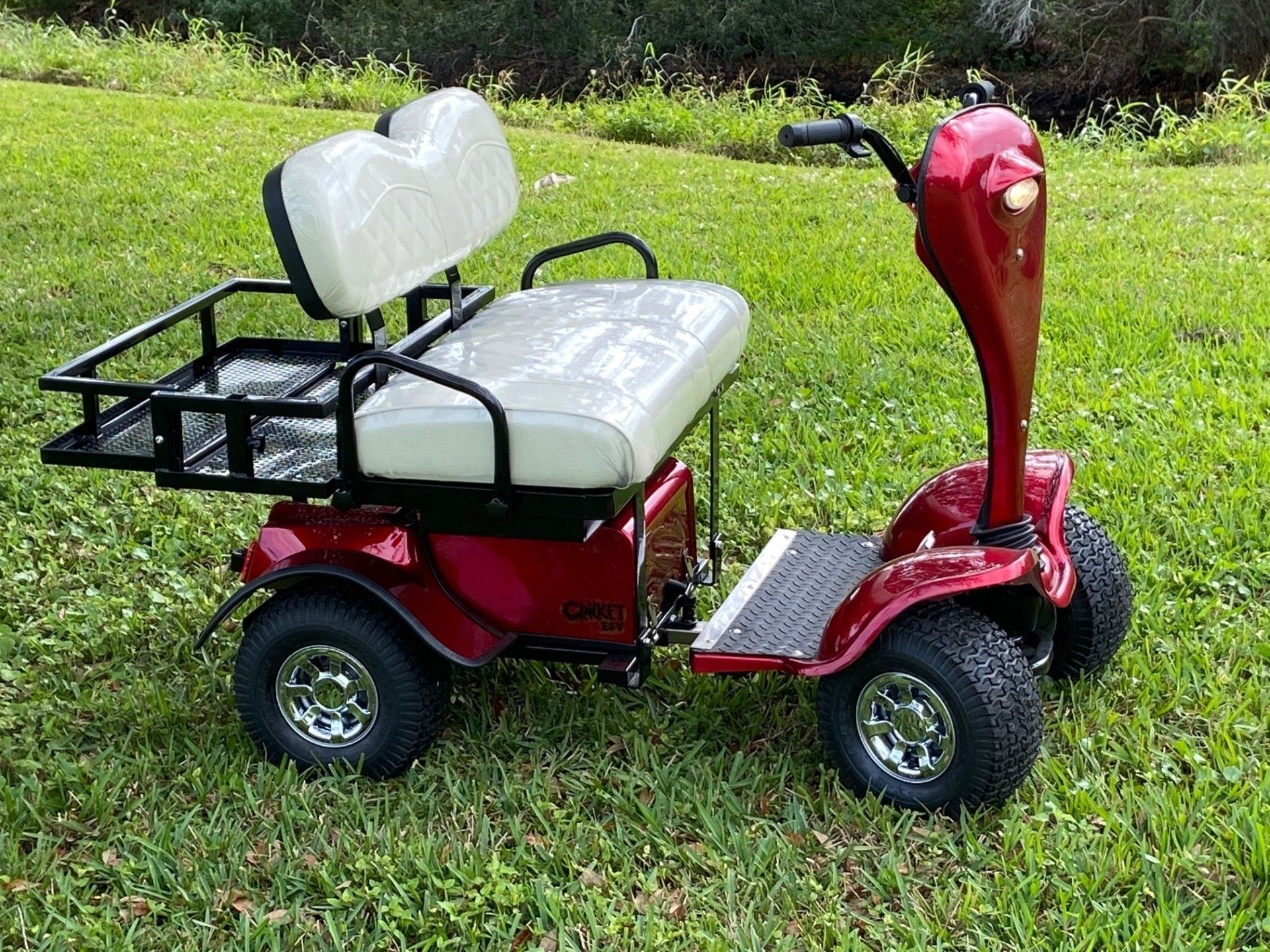 A red golf cart with a white seat is parked in the grass.