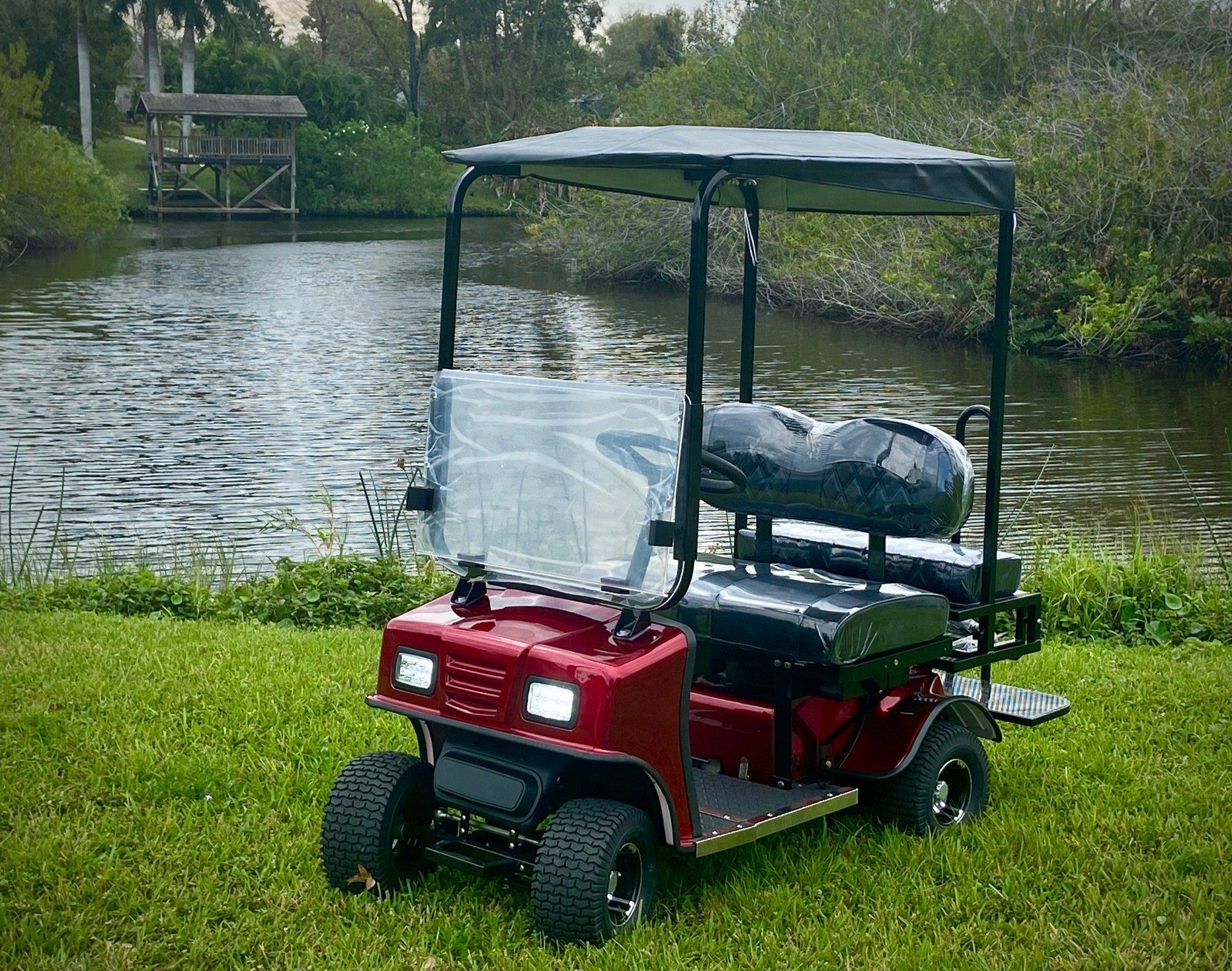 A red golf cart is parked in the grass next to a body of water.