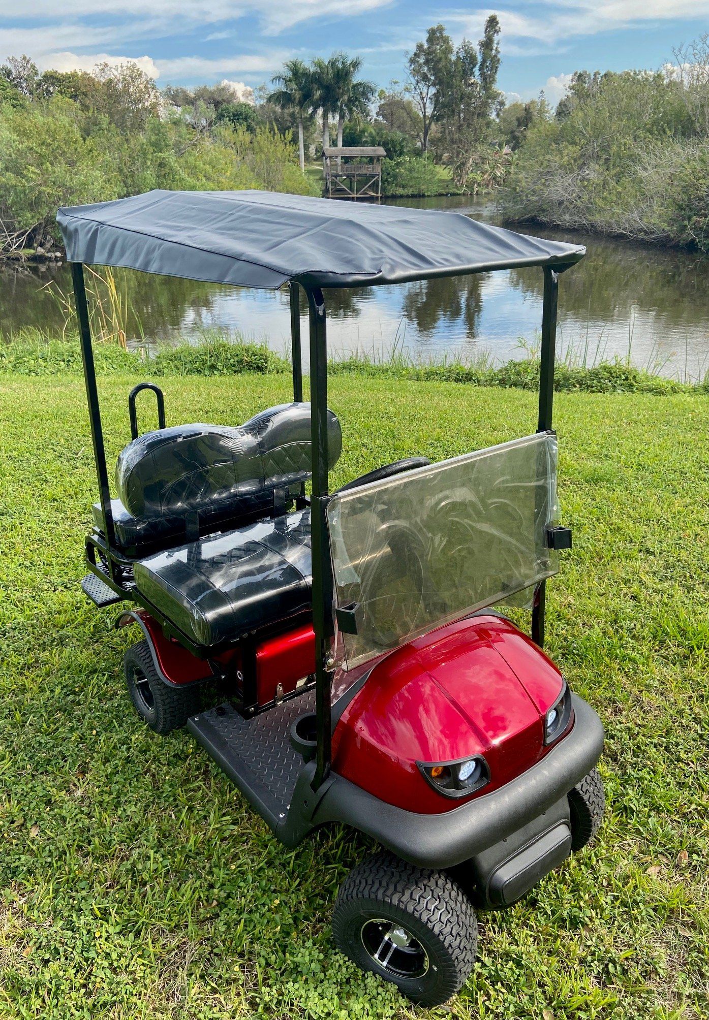 A red golf cart is parked in the grass next to a body of water.