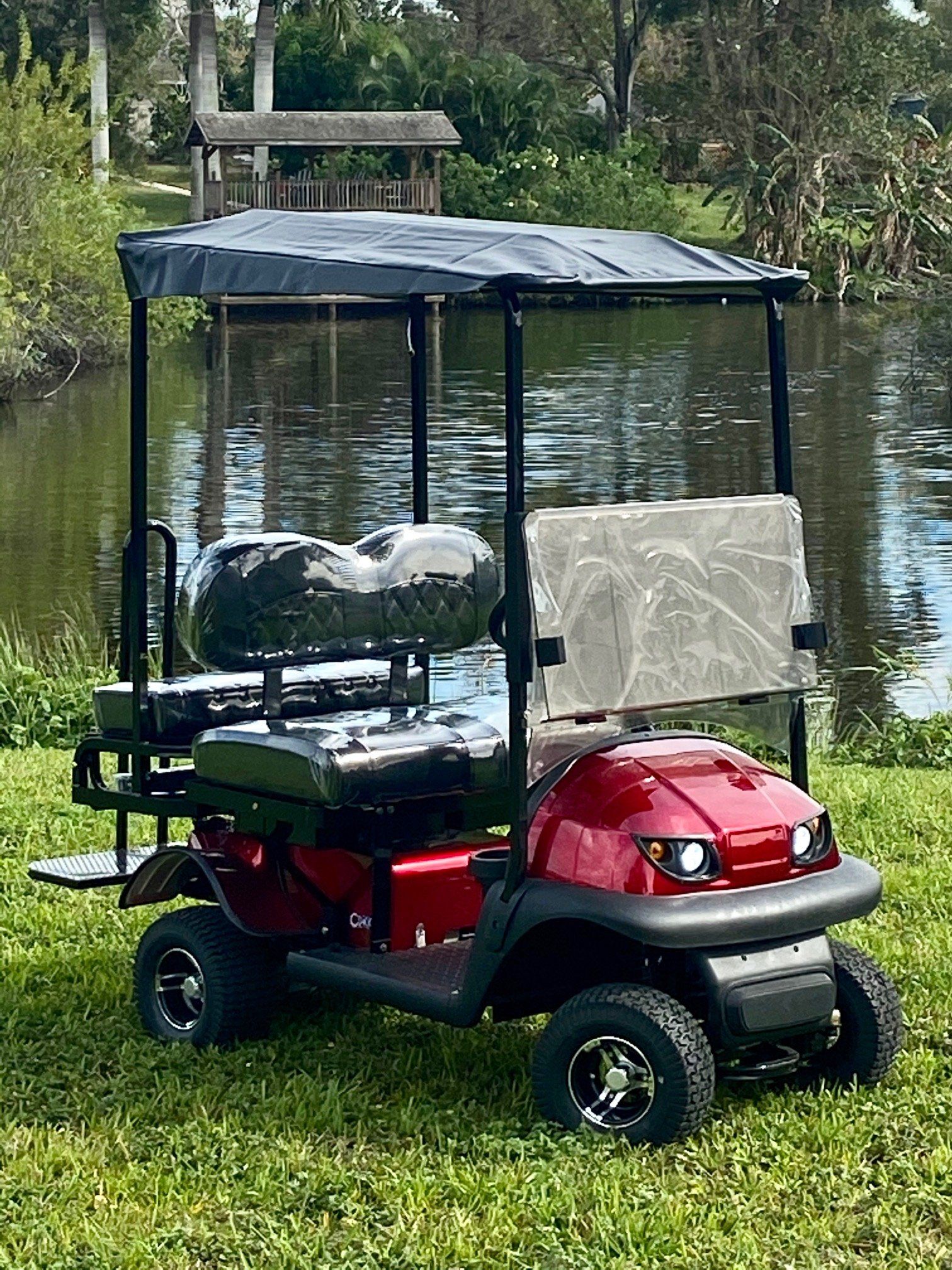A red golf cart with a canopy is parked in the grass near a lake.