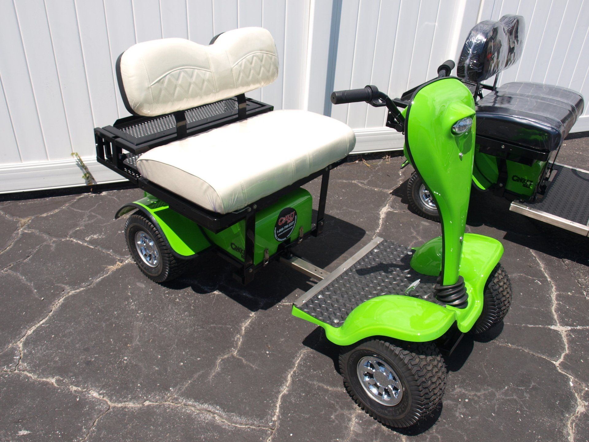 A green golf cart with a white seat is parked in front of a white fence.