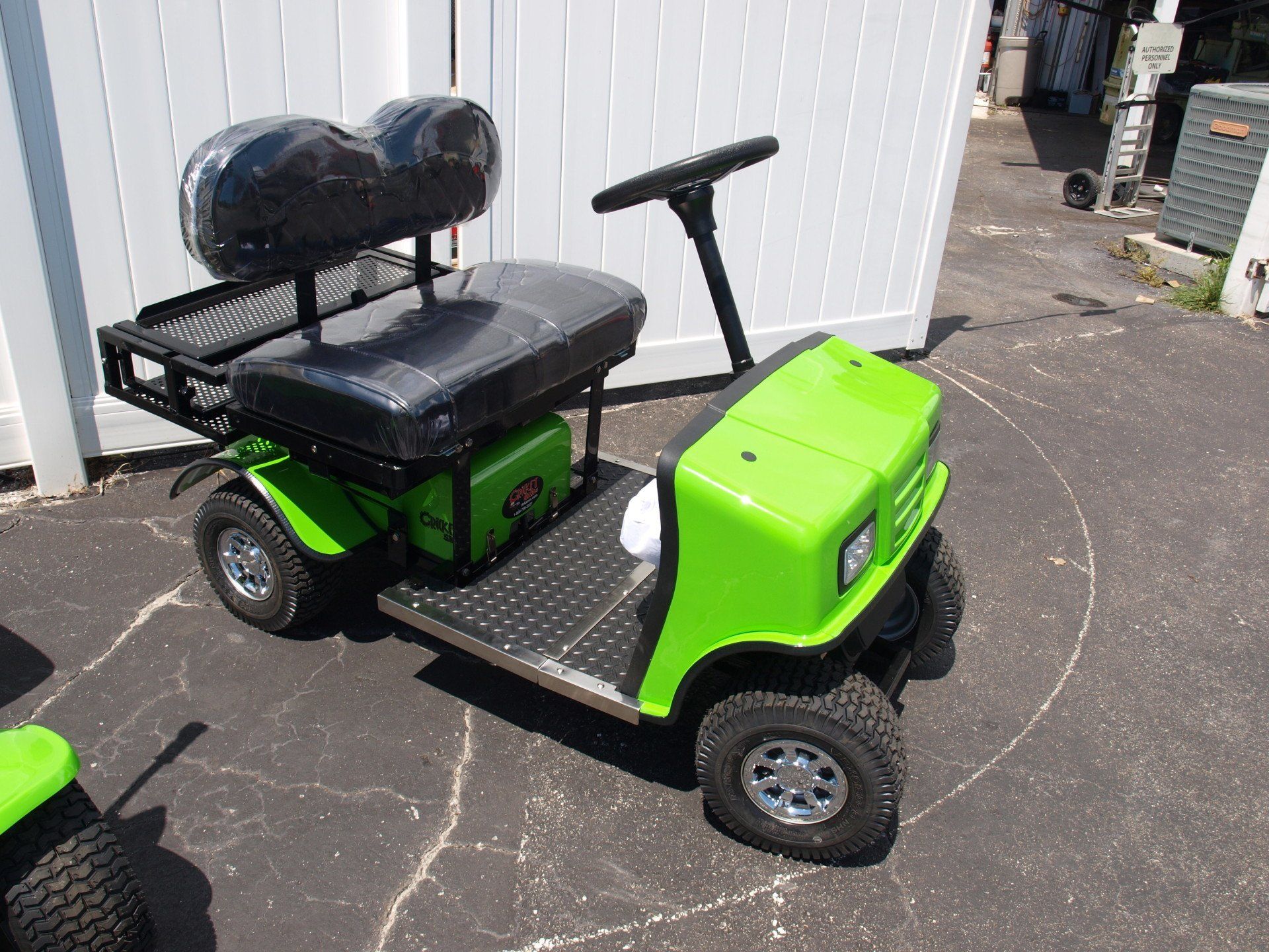 A green golf cart is parked in front of a white fence.