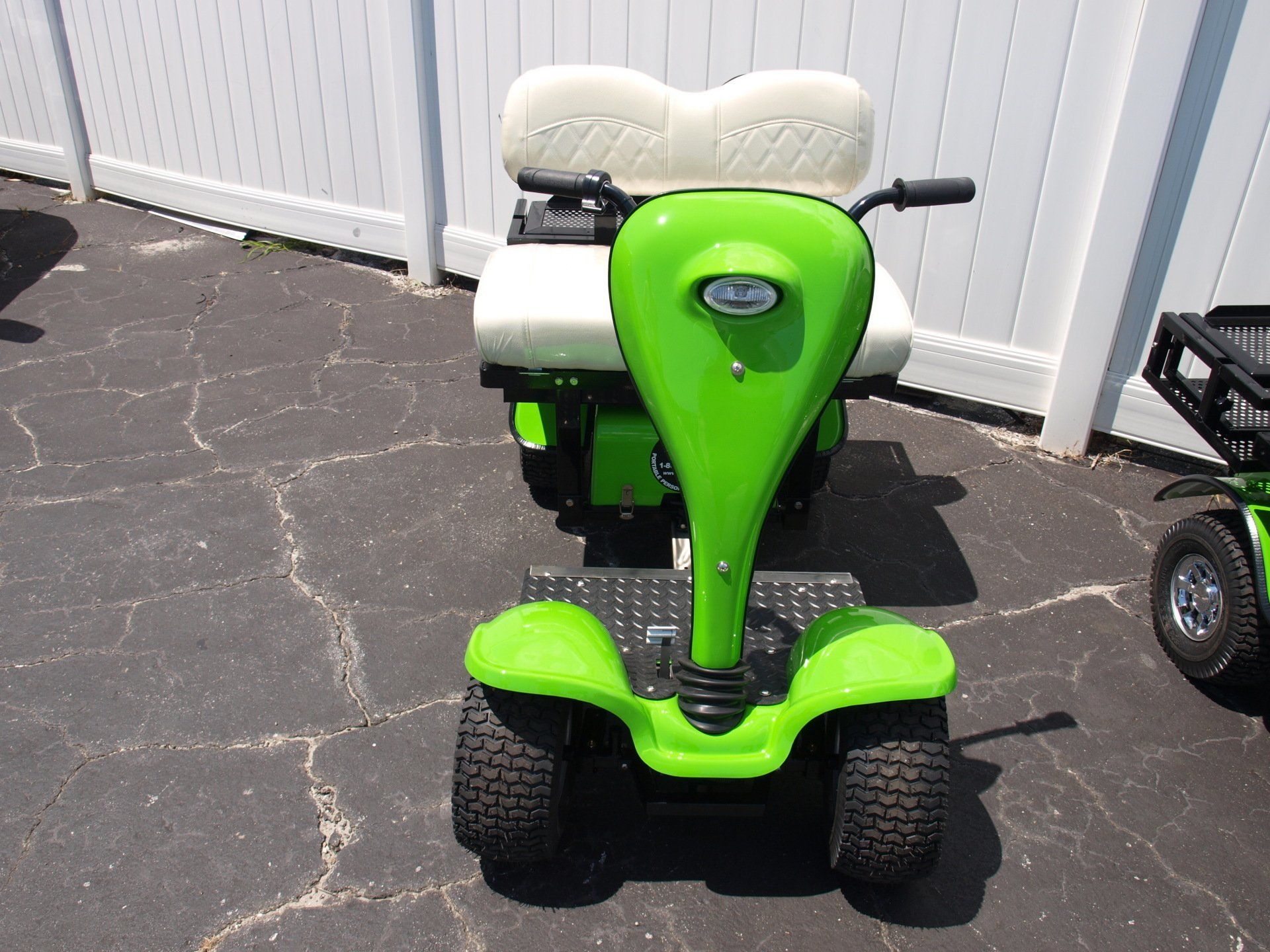 A green golf cart is parked in front of a white fence
