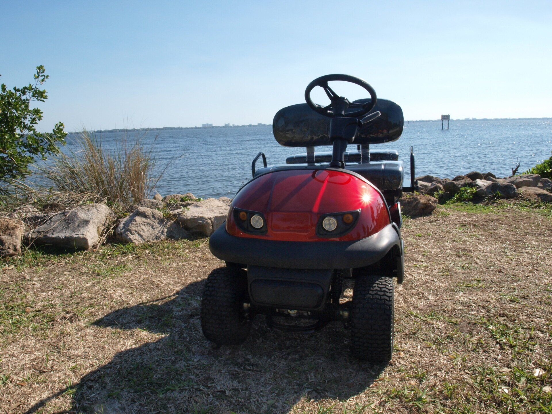 A red golf cart is parked in front of a body of water