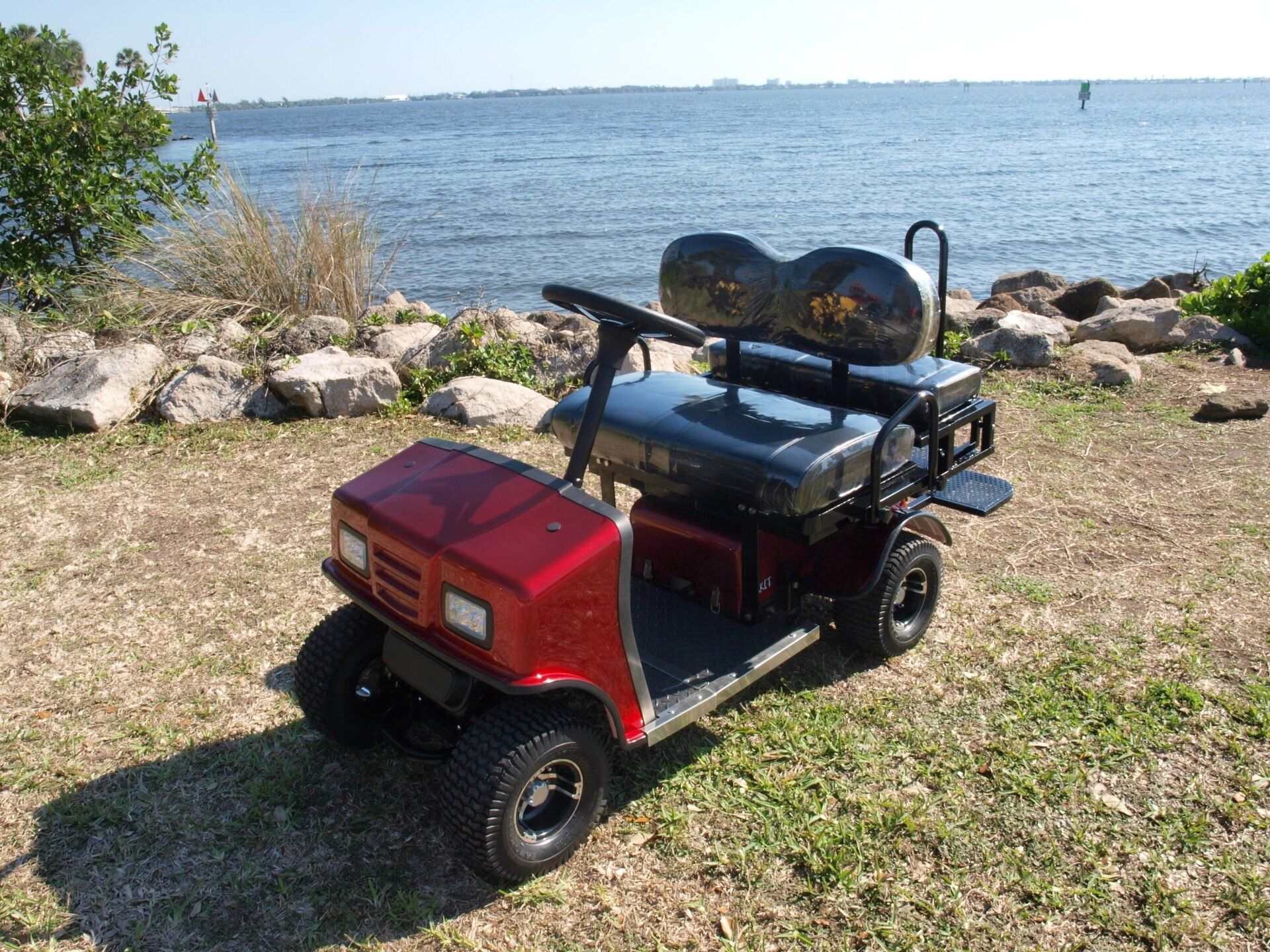 A red golf cart is parked in front of a body of water.
