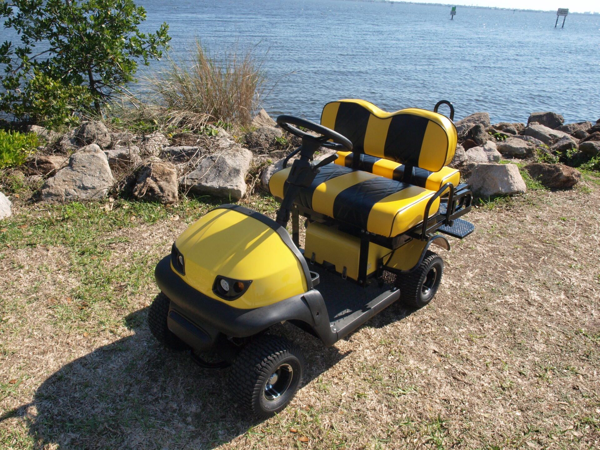 A yellow and black golf cart is parked in front of a body of water.