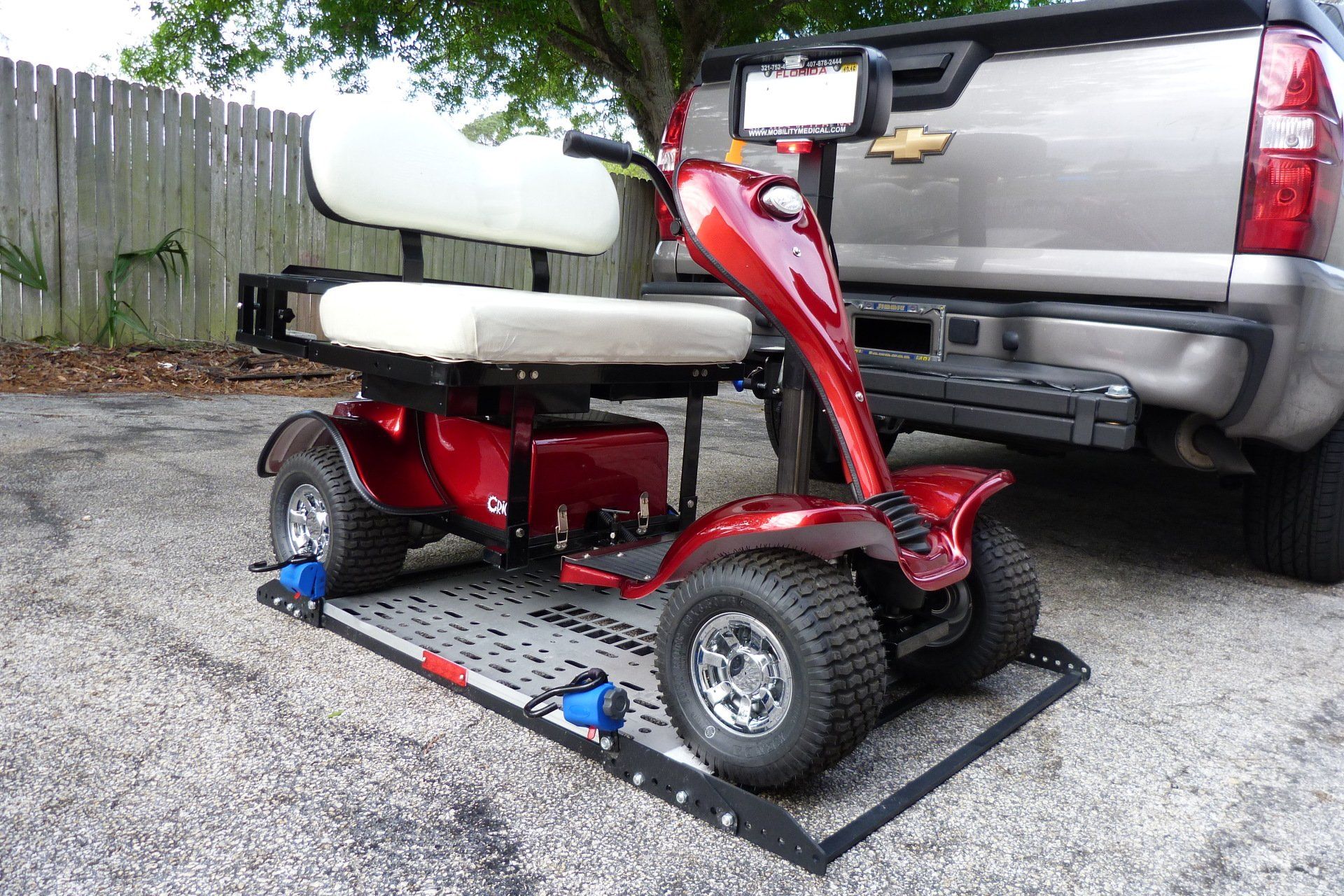 A red mobility scooter is parked next to a silver truck