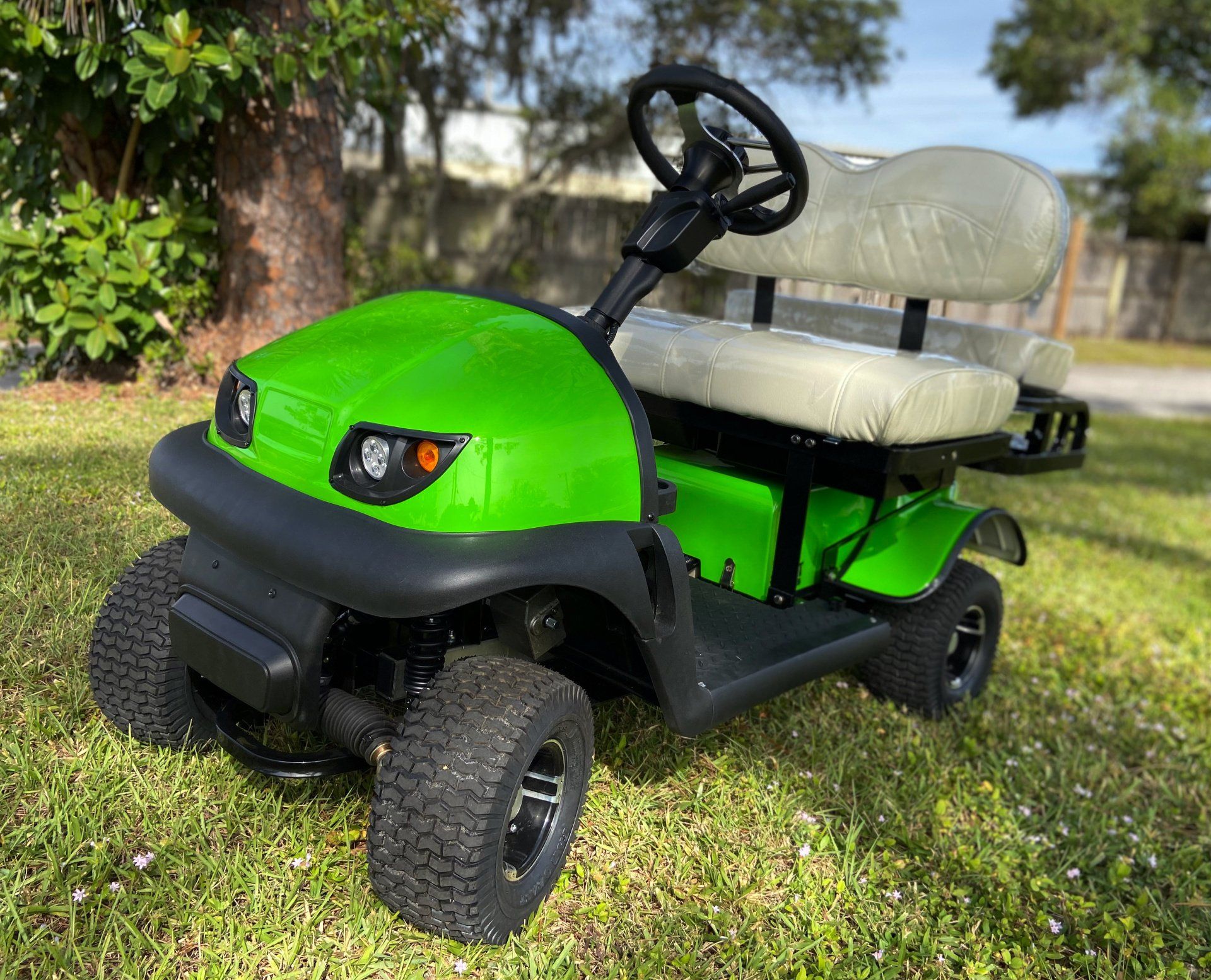A green golf cart is parked in the grass next to a tree.