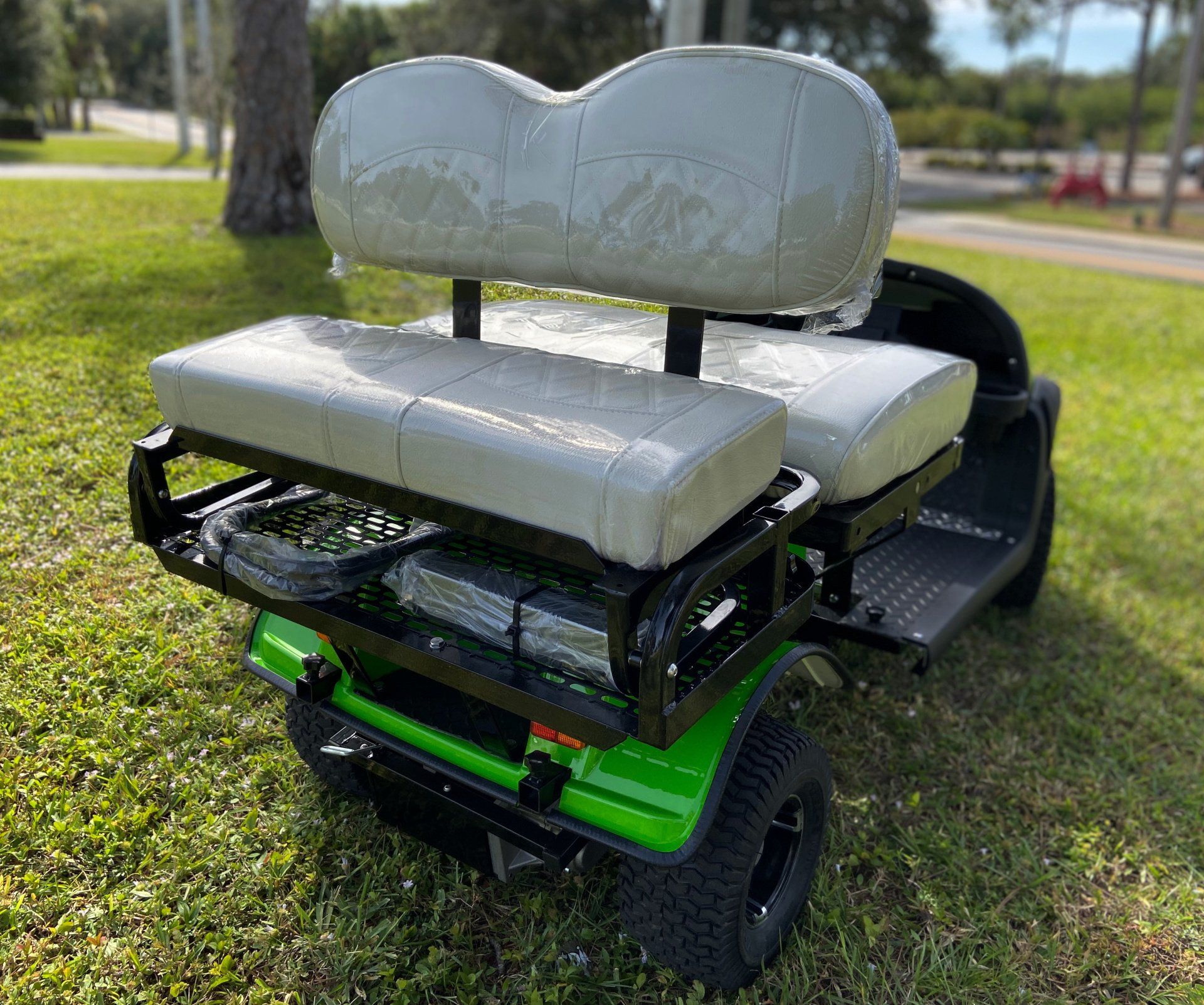 A green golf cart with white seats is parked in the grass.