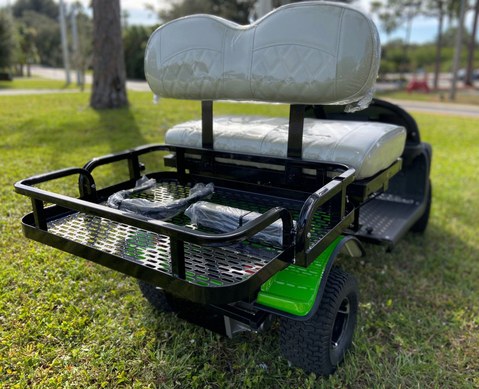 A green and white golf cart is parked in the grass.