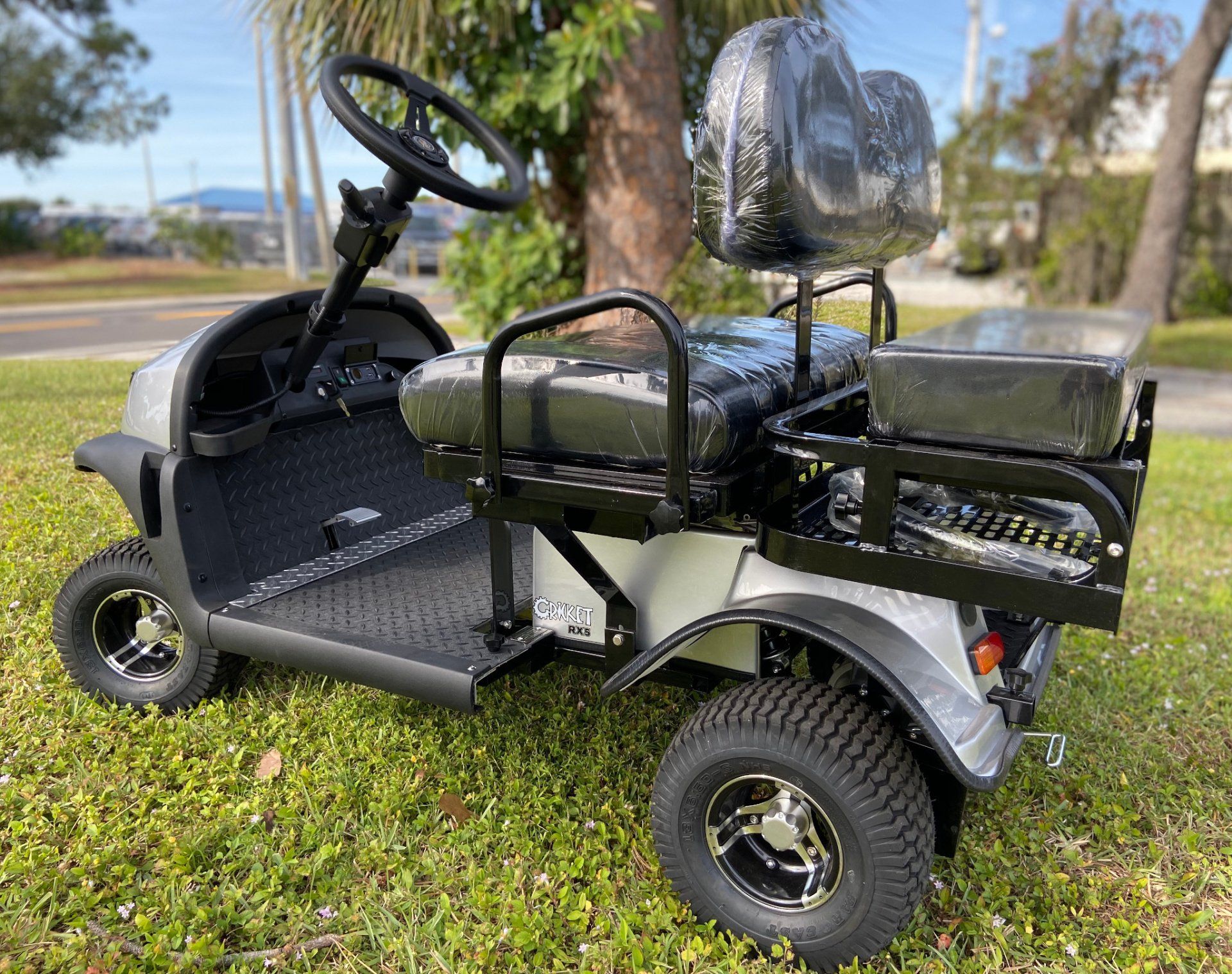 A golf cart is parked in the grass next to a tree.