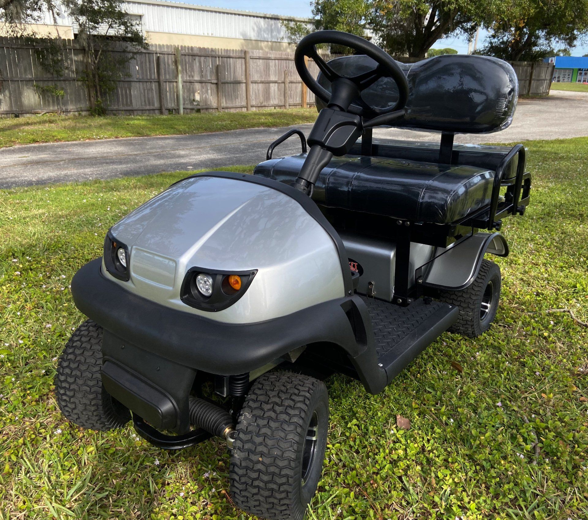 A silver and black golf cart is parked in the grass.