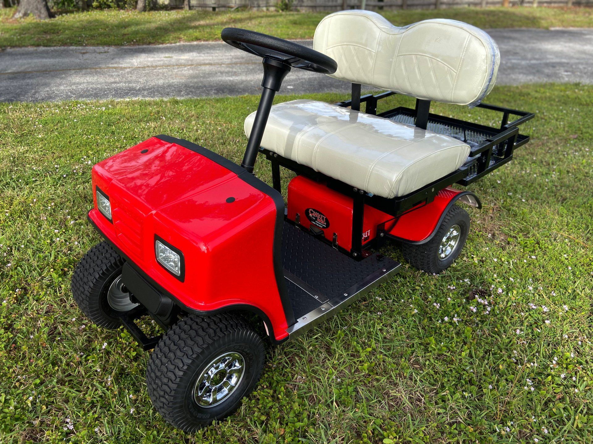 A red golf cart with white seats is parked in the grass.