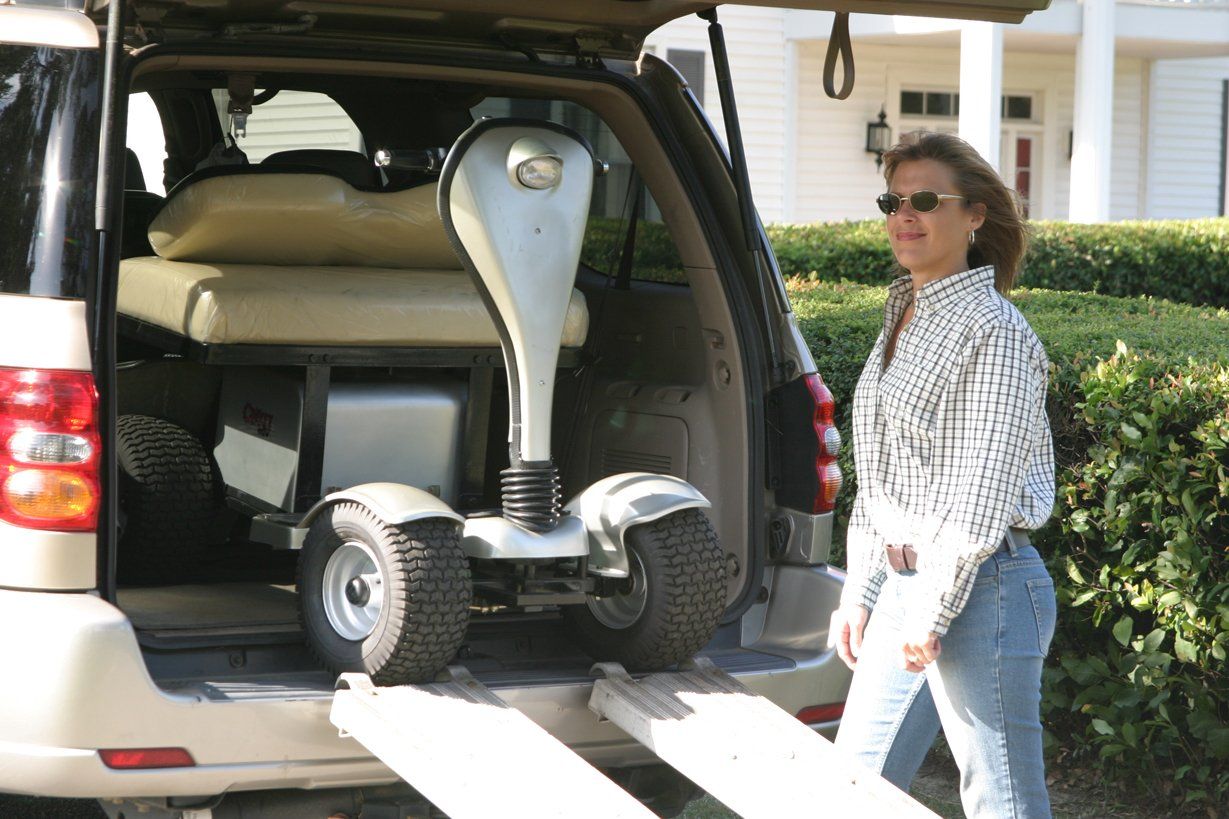 A woman is loading a mobility scooter into the back of a suv