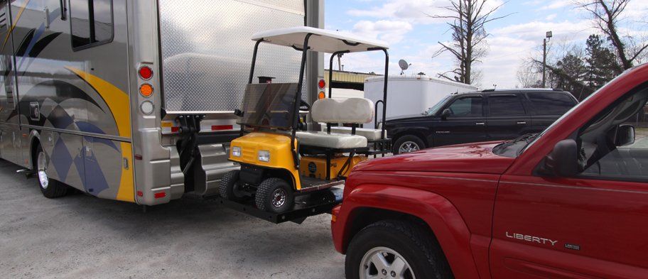 A red truck is towing a golf cart next to a rv.