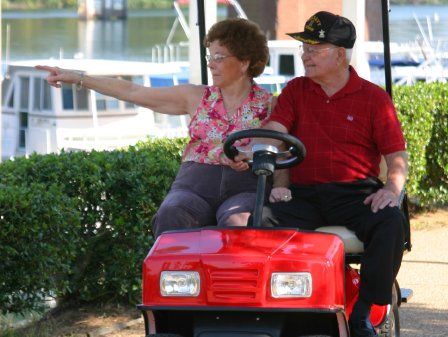 A man and a woman are riding a red golf cart