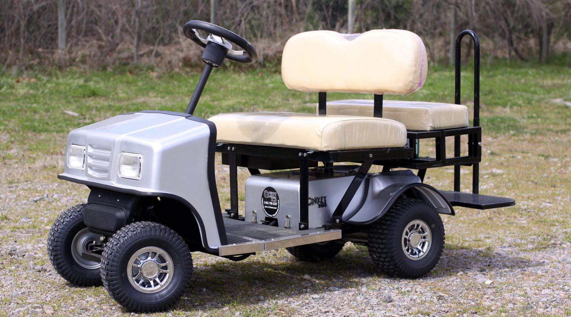 A silver golf cart with white seats is parked in a gravel lot.