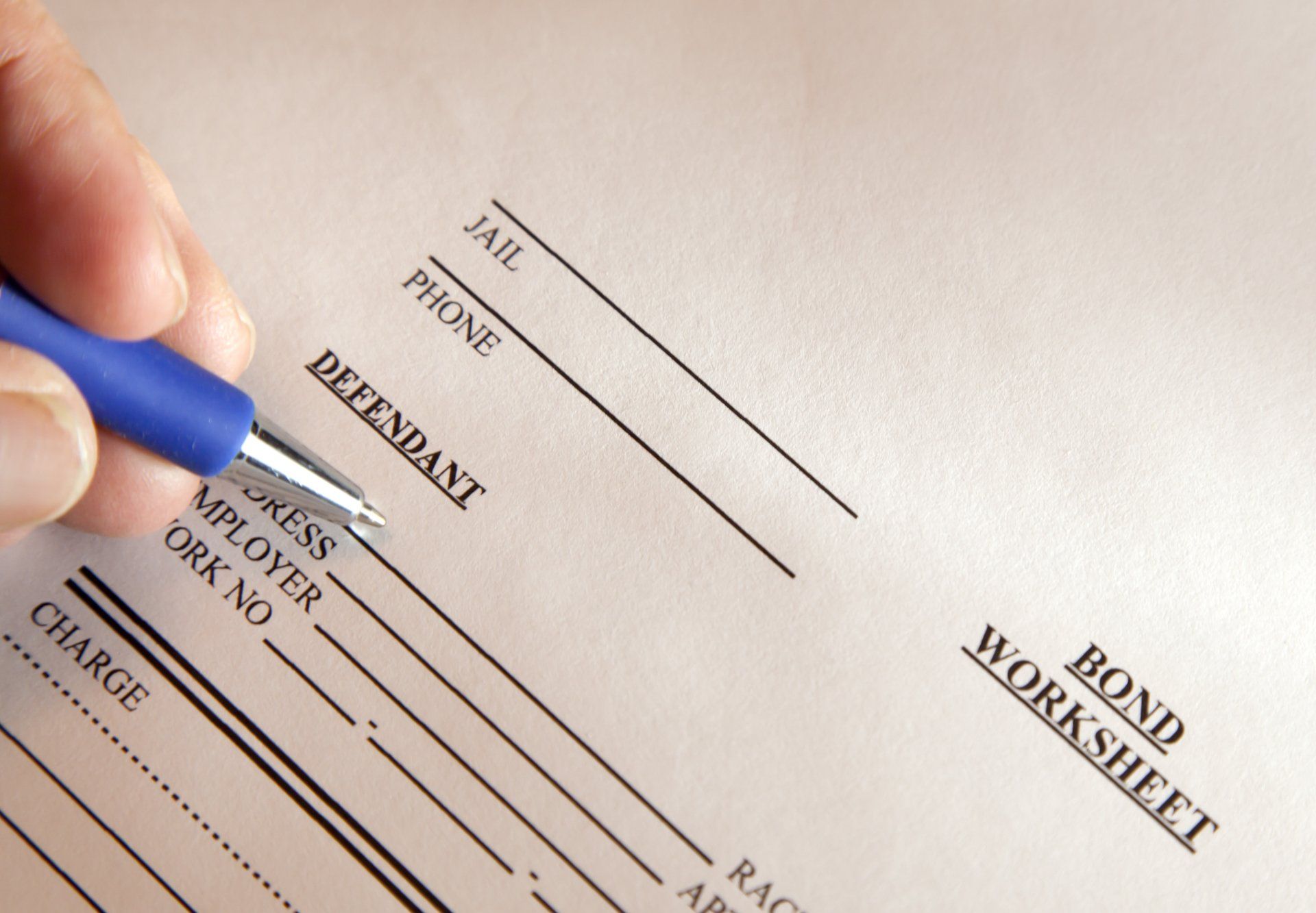 Person signing rapid intake bond paperwork in Pensacola, FL Hand filling out a bond worksheet with a blue pen. The form lists fields like