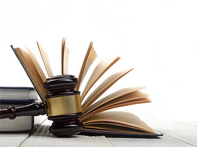 Wooden gavel resting on an open book, with other books visible. White background and wooden table.