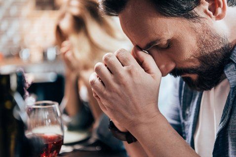 Man Praying — Pensacola / Milton Florida — Matt Mckeehan Bail Bonds A man with closed eyes presses his hands together, seemingly in prayer or distress, at a table; a woman is in the background.