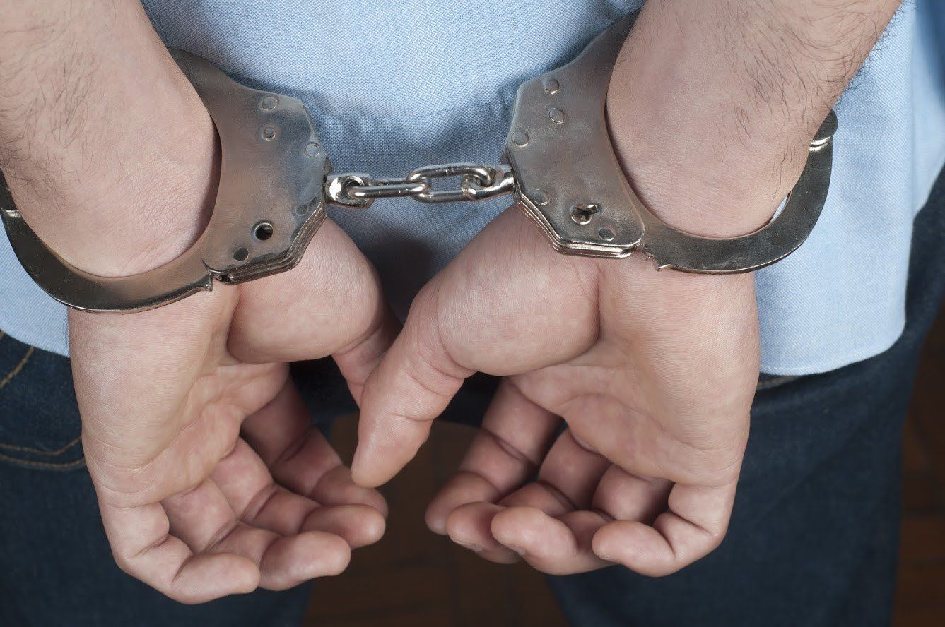 Hands in handcuffs, person wearing light blue shirt and jeans.
