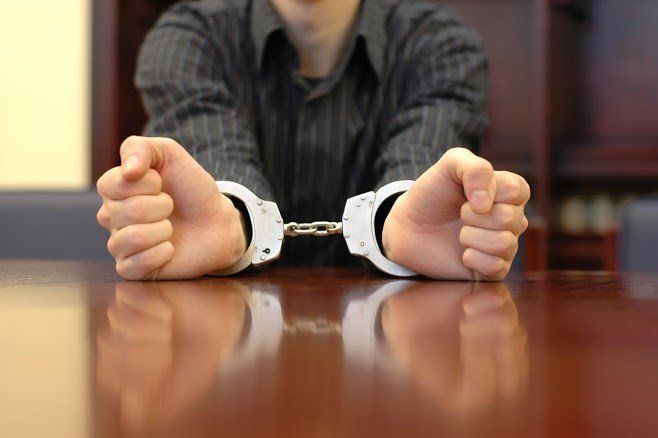 Man With Handcuffs — Pensacola, FL — Matt Mckeehan Bail Bonds Person in handcuffs with hands resting on a polished wooden surface.